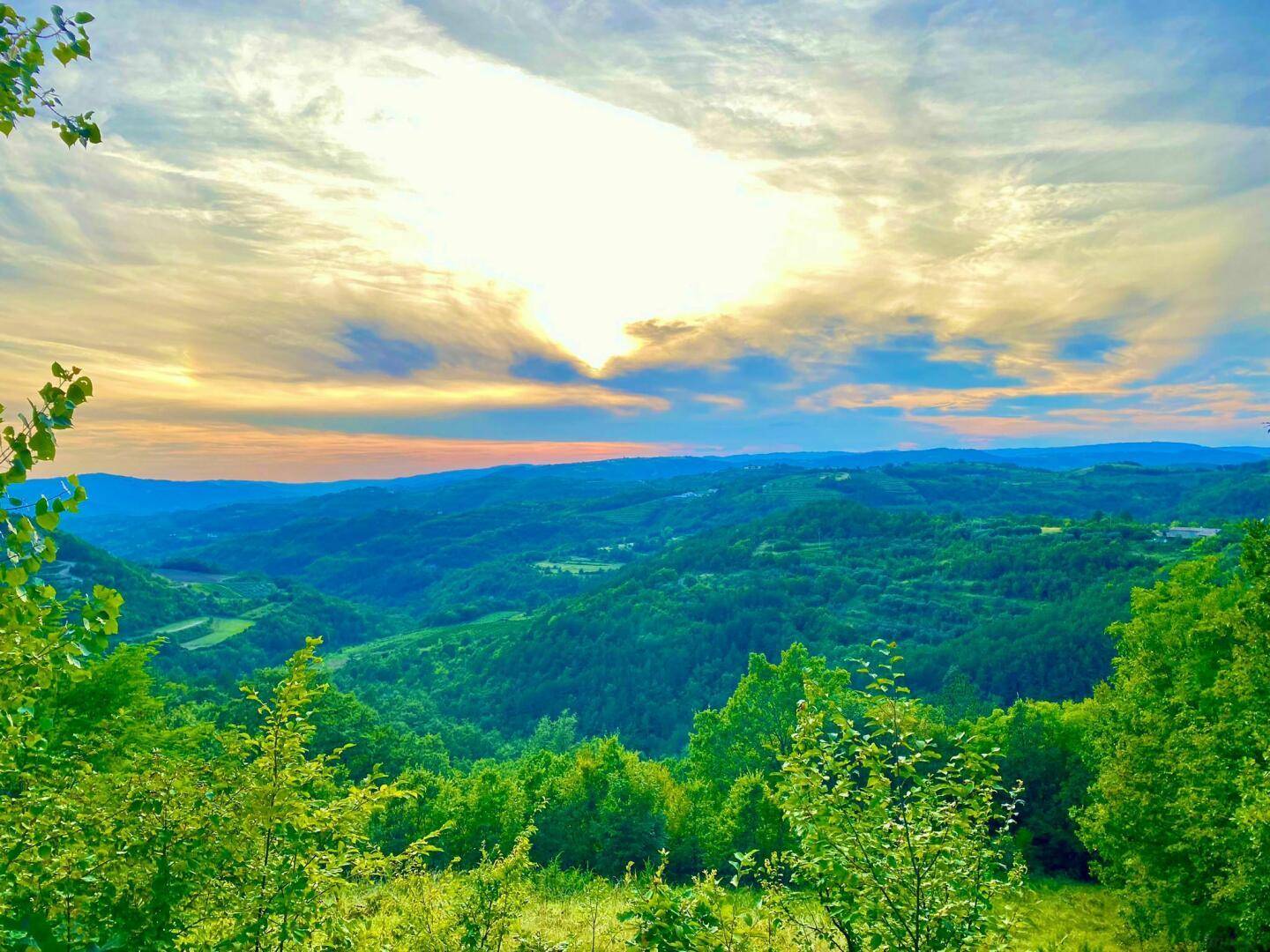 Atemberaubender Panoramablick über eine weite, grüne Hügellandschaft unter einem dramatischen Himmel.