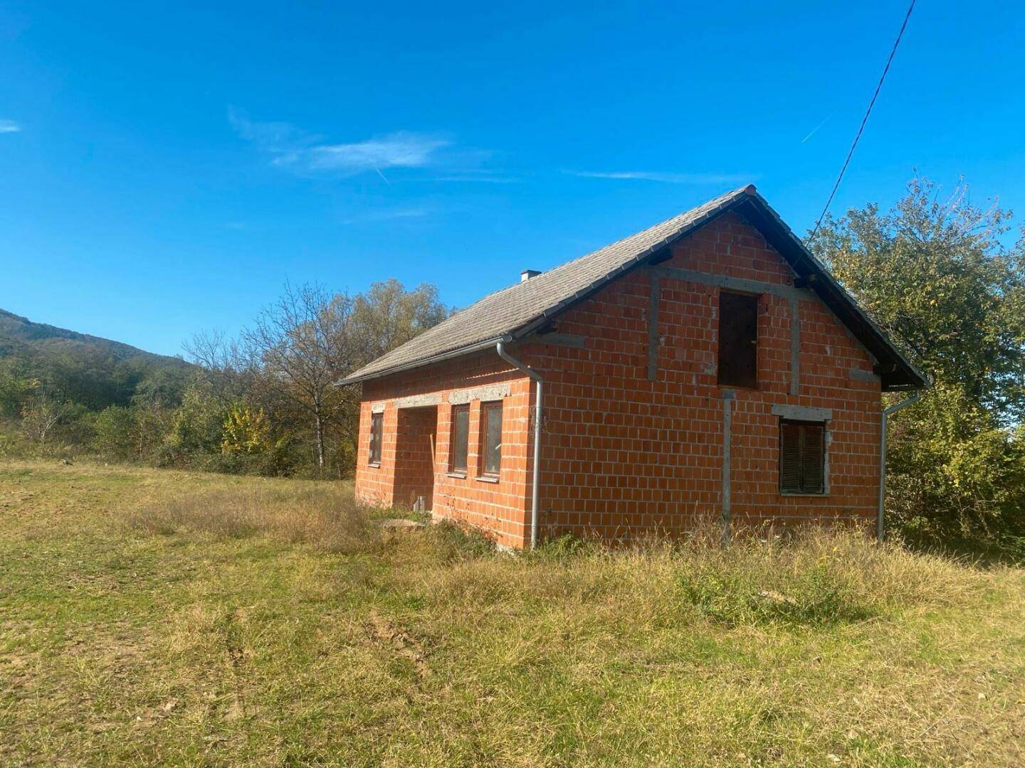 Freistehendes Ziegelhaus mit Satteldach auf einem großen, grasbewachsenen Grundstück.