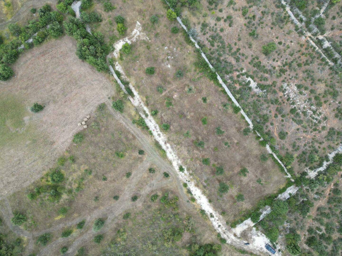 Luftaufnahme eines weitläufigen, trockenen Grundstücks mit spärlicher Vegetation und alten Steinmauern, umgeben von Natur.
