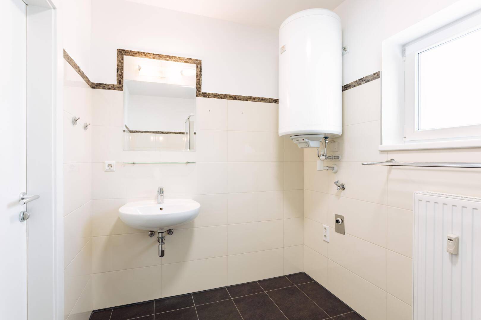 Badezimmer mit Waschbecken, Spiegel und Warmwasserboiler, ausgestattet mit Fliesen.