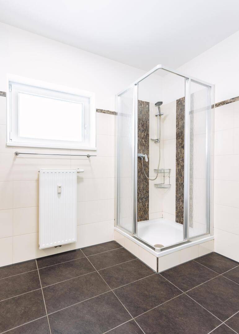 Modernes Badezimmer mit Duschkabine, dunklen Bodenfliesen und einem Fenster für Tageslicht.
