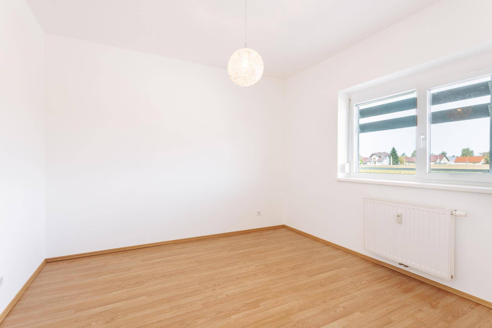 Geräumiges Schlafzimmer mit Laminatboden, weiß gestrichenen Wänden und einem großen Fenster.