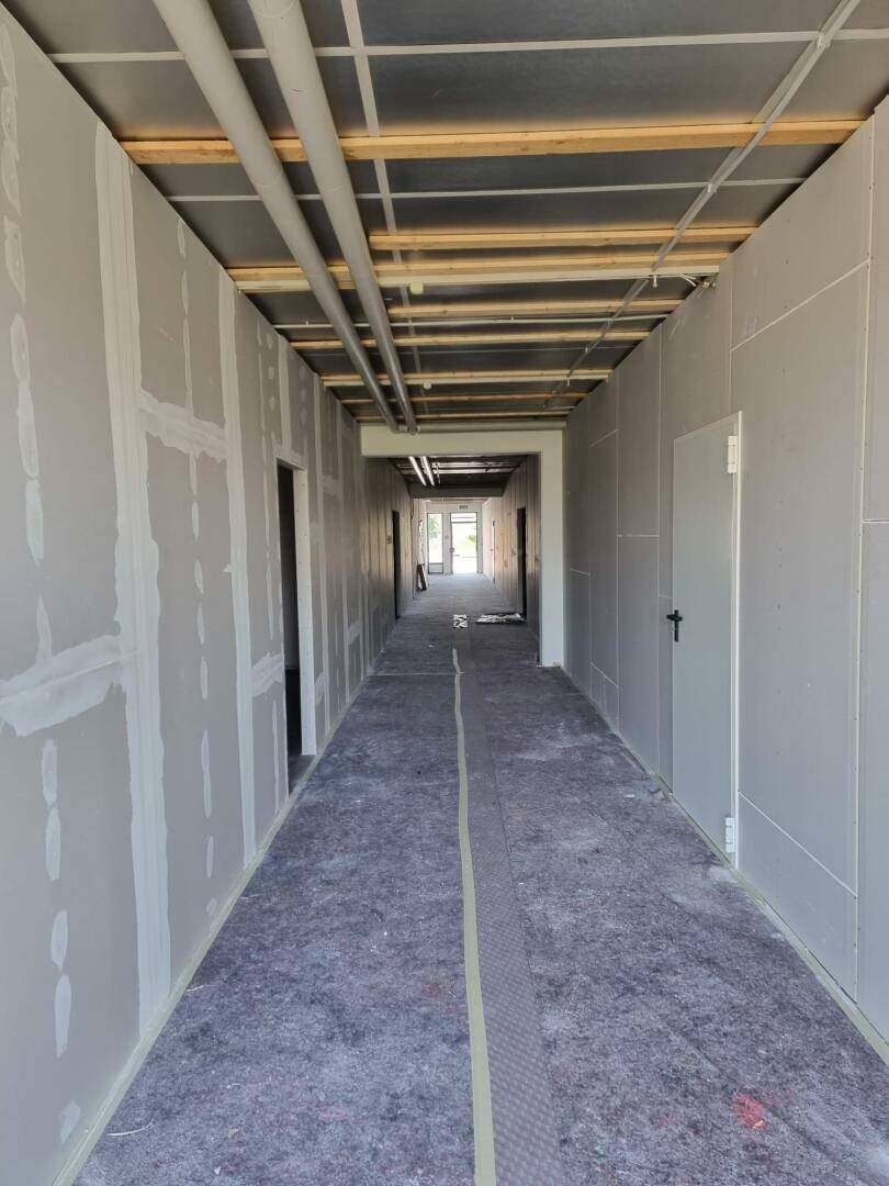 Langer Flur in einem Neubau während der Bauphase mit unverputzten Wänden und sichtbaren Deckeninstallationen.