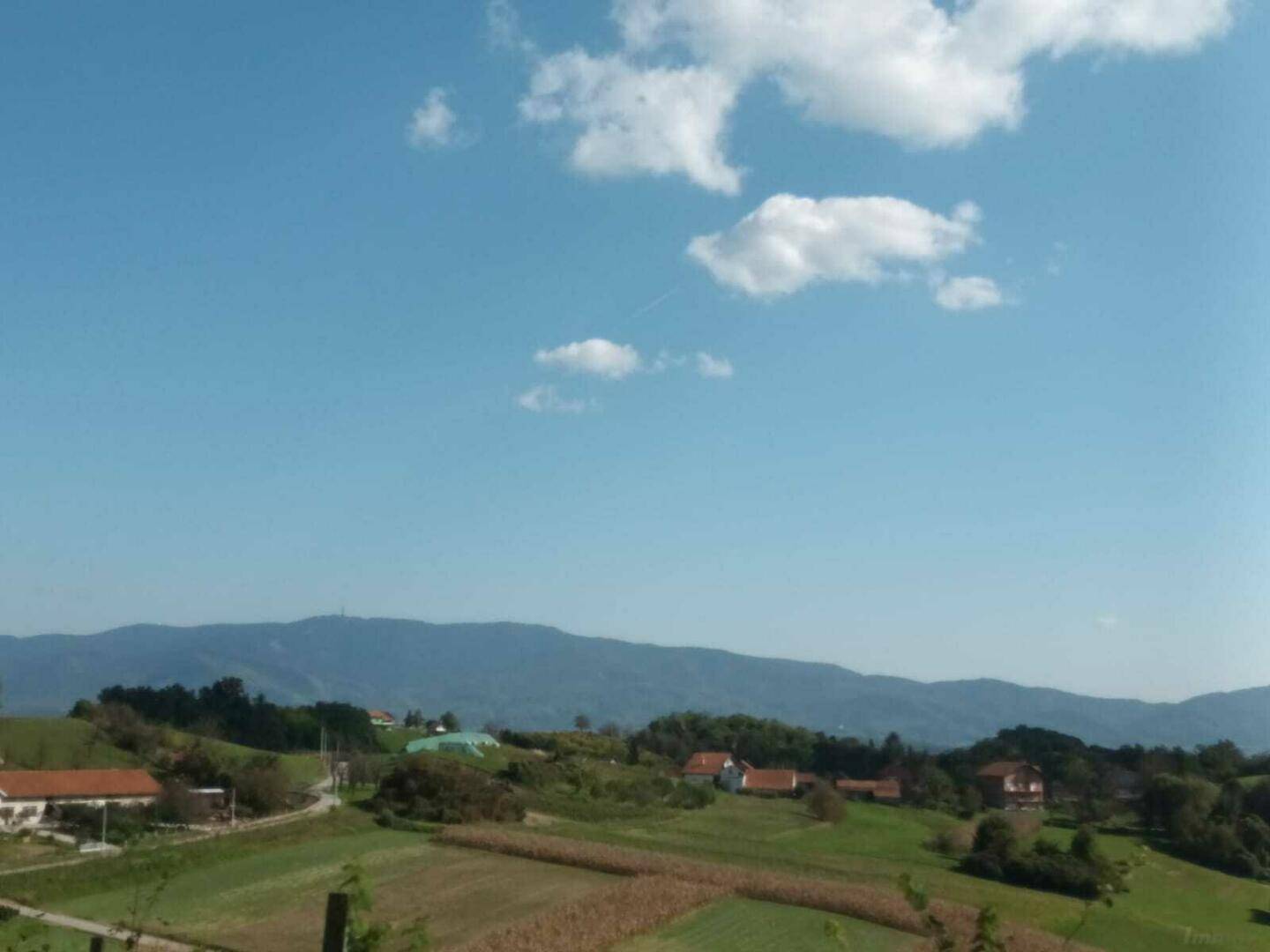 Panoramablick über eine weite grüne Landschaft mit Bergen und einem Dorf in der Ferne.