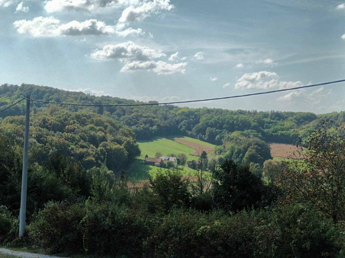 Malerische ländliche Szene mit bewaldeten Hügeln und einem kleinen Gehöft im Tal.