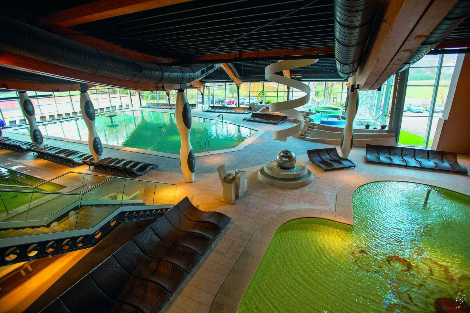 Moderner Wellnessbereich mit großzügigen Schwimmbecken, einer Wasserrutsche und bequemen Liegestühlen.