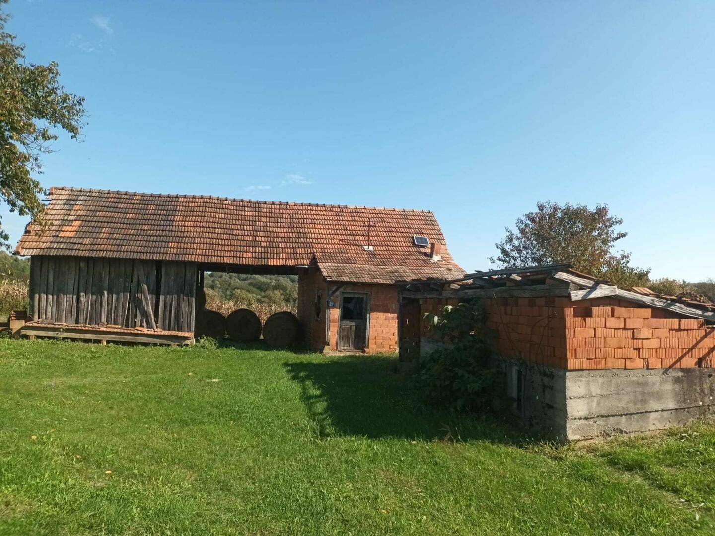 Rustikale Scheune mit Ziegeldach und einem Anbau aus Ziegelsteinen auf einer grünen Wiese.