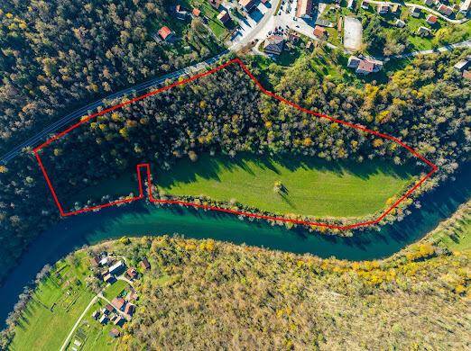 Luftbild einer Flussbiegung mit Wald und Wiesen, umrandet von einer roten Grundstücksgrenze.
