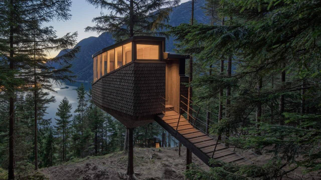 Modernes Baumhaus-Design mit Holzfassade und großen Fenstern, eingebettet in einen Wald mit Seeblick.