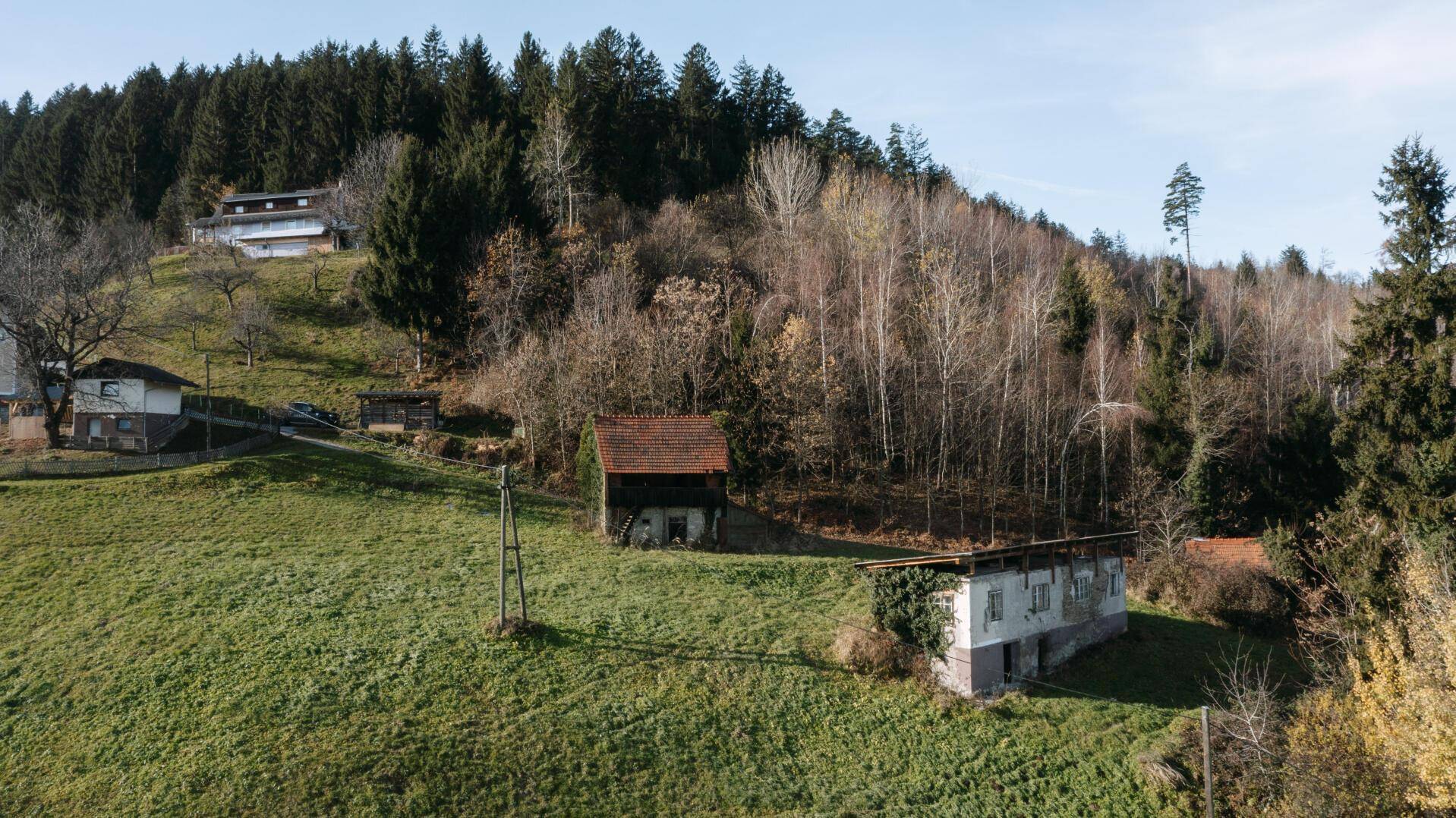 Blick auf eine grüne Hügellandschaft mit traditionellen Häusern und dichtem Baumbestand unter klarem Himmel.