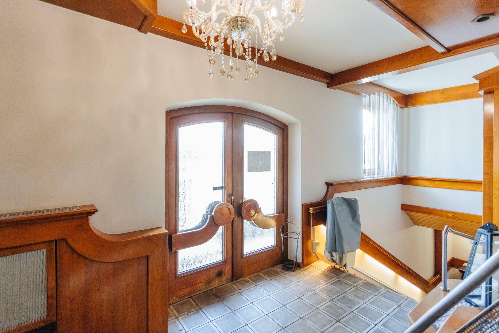 Eingangsbereich mit Holztüren, Fliesenboden und einer eleganten Kristallleuchte.