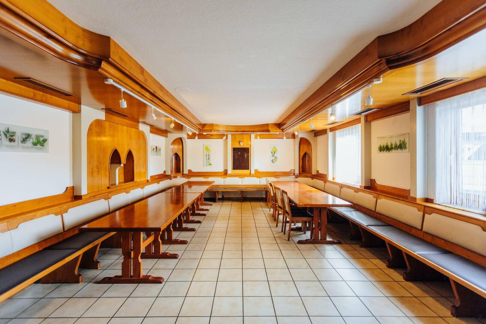 Großer Speisesaal mit langen Holztischen und Bänken, ideal für größere Gesellschaften.