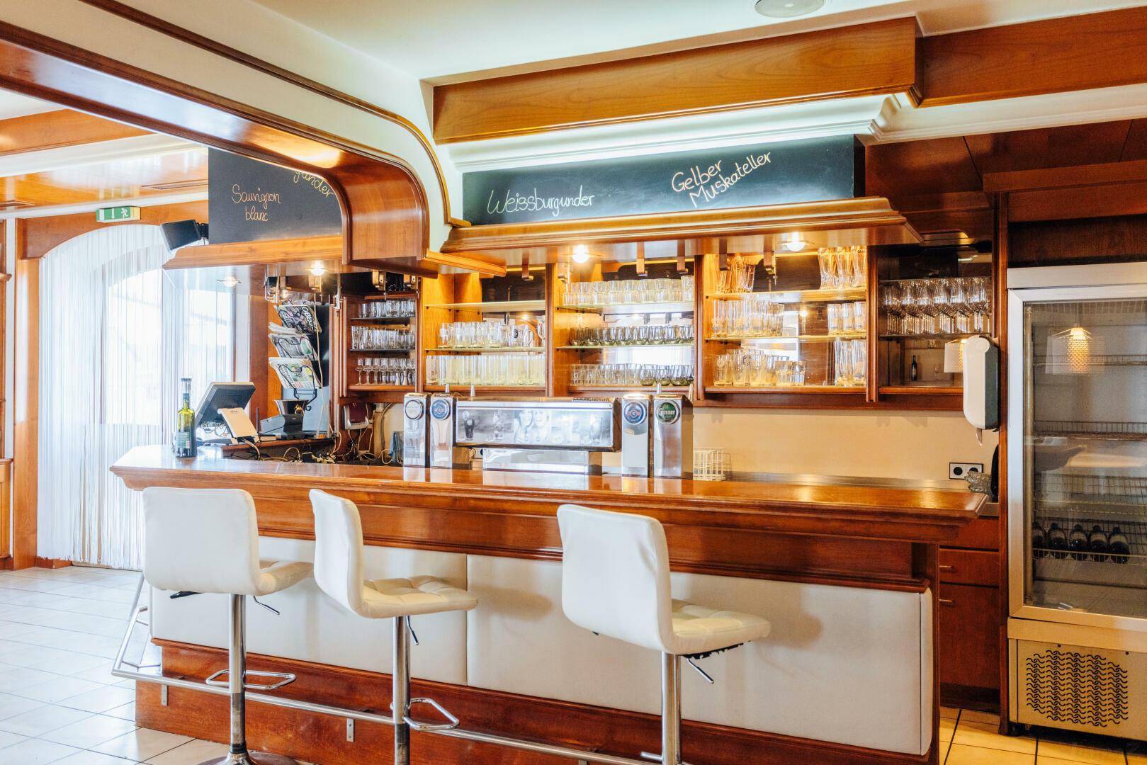 Gut ausgestattete Bar mit Holztheke, Barhockern und vielen Gläsern in den Regalen.