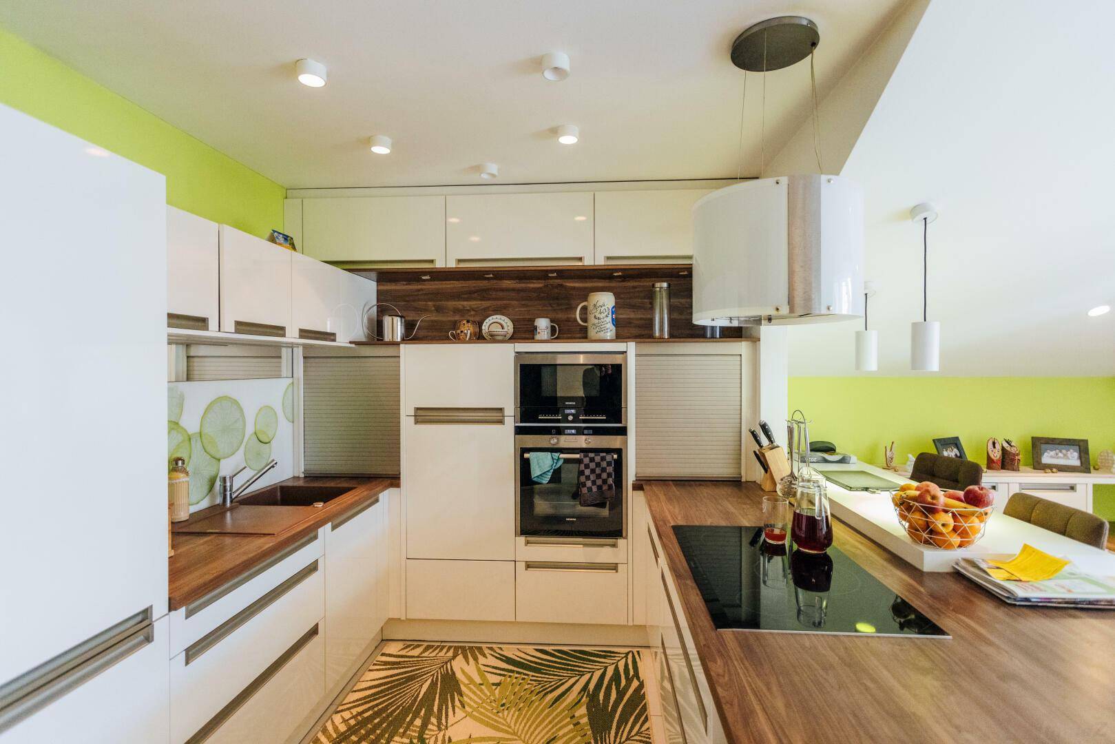 Moderne Küche mit weißen Schränken, Holz-Arbeitsplatten und grüner Akzentwand.