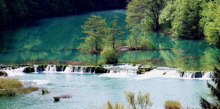 Atemberaubender Blick auf einen Fluss mit türkisfarbenem Wasser und kleinen Kaskaden inmitten üppiger Natur.