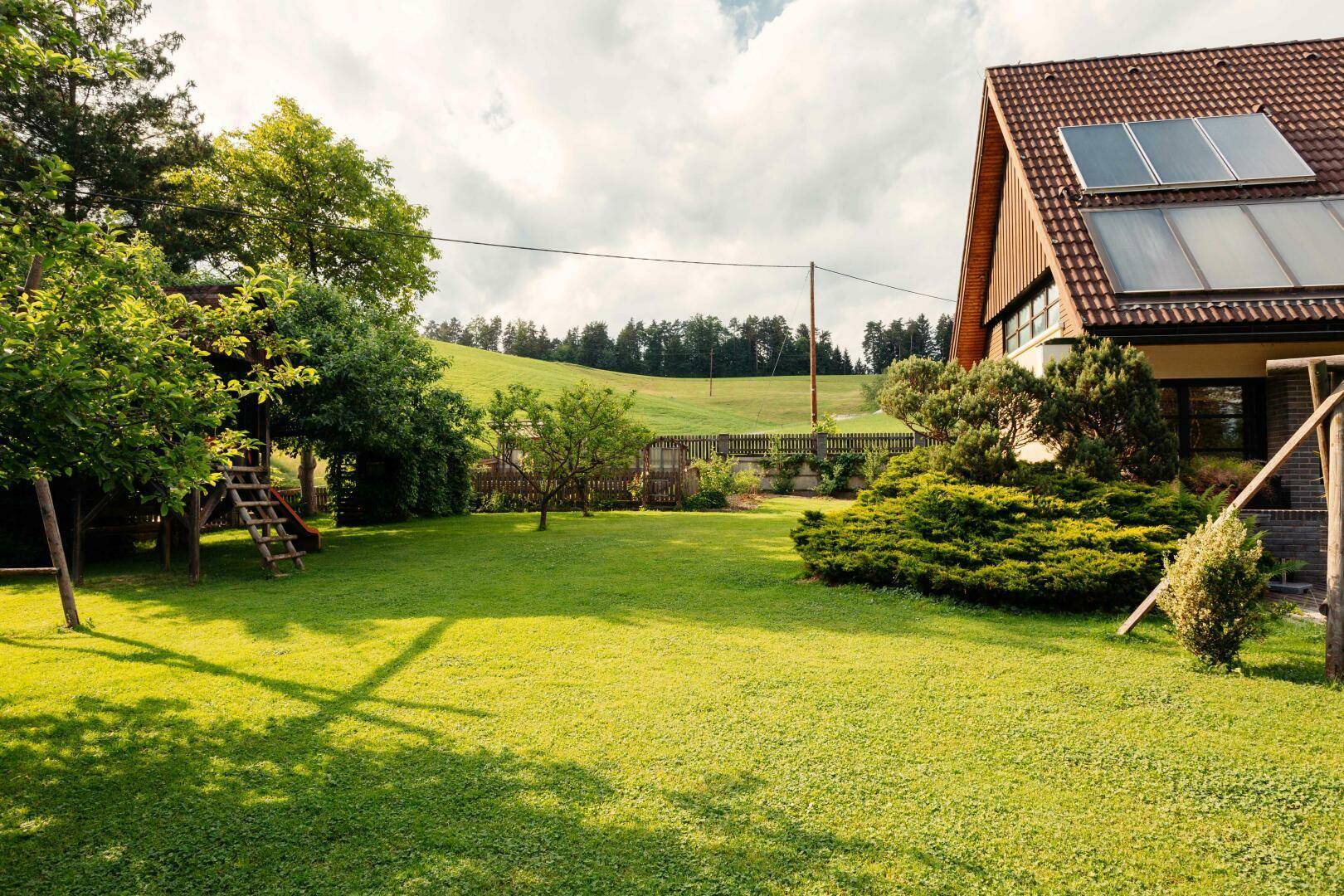 Großer Garten mit Rasenfläche, Spielturm und dem Haus mit Solaranlage im Hintergrund.