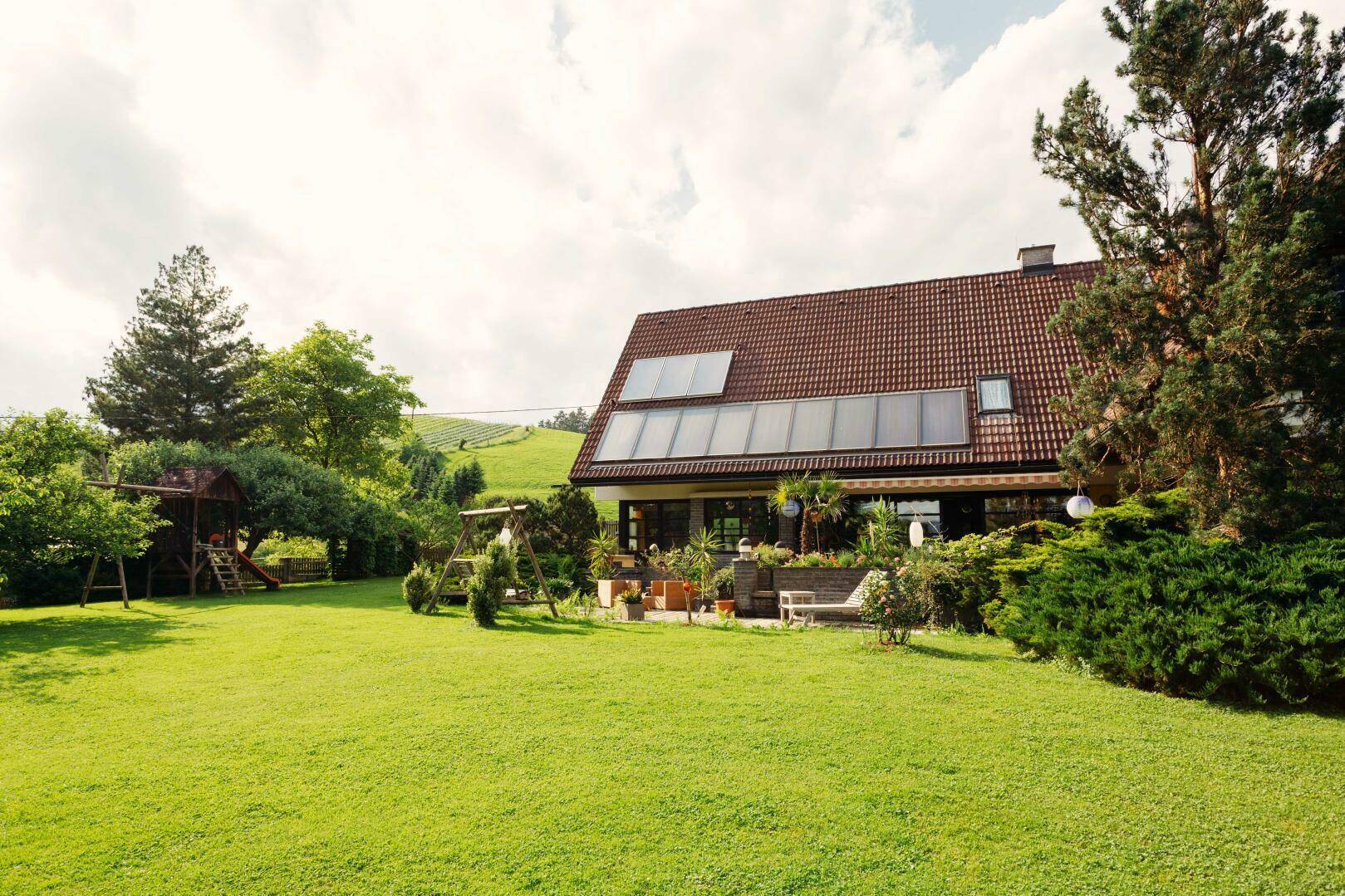 Großer Garten mit Rasenfläche, Schaukel und Spielplatz, das Haus mit Solaranlage.