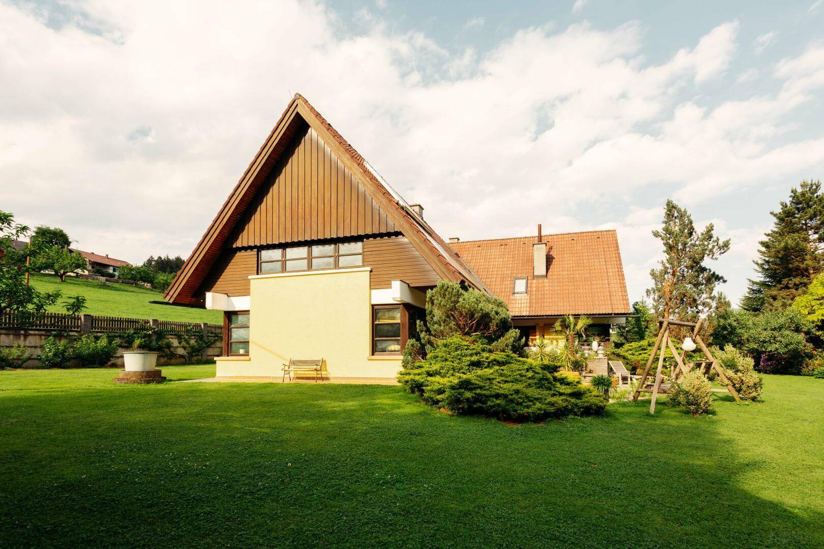 Seitenansicht des Hauses mit großem Rasen, Bäumen und einer Holzschaukel im Garten.