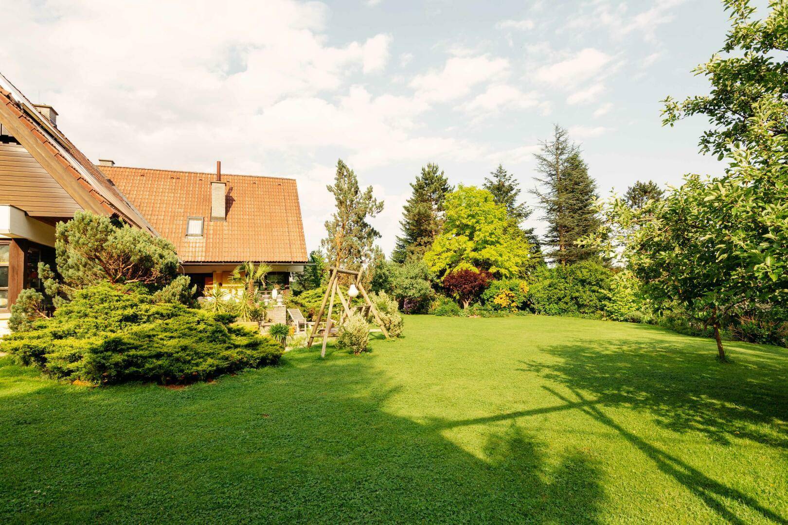 Große, gepflegte Rasenfläche mit Bäumen und dem Haus im Hintergrund, ideal zum Entspannen.