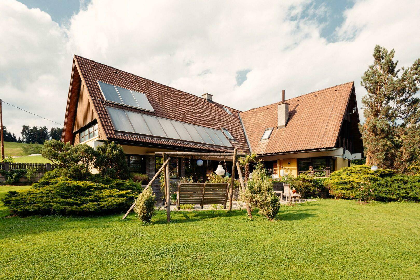 Weitläufiger Rasenbereich mit einer Holzschaukel und dem Haus mit Solarpaneelen auf dem Dach.