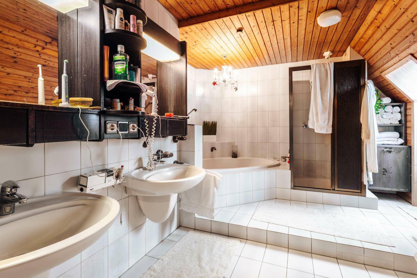Geräumiges Badezimmer mit Doppelwaschbecken, Badewanne und Duschkabine unter Holzdachschräge.