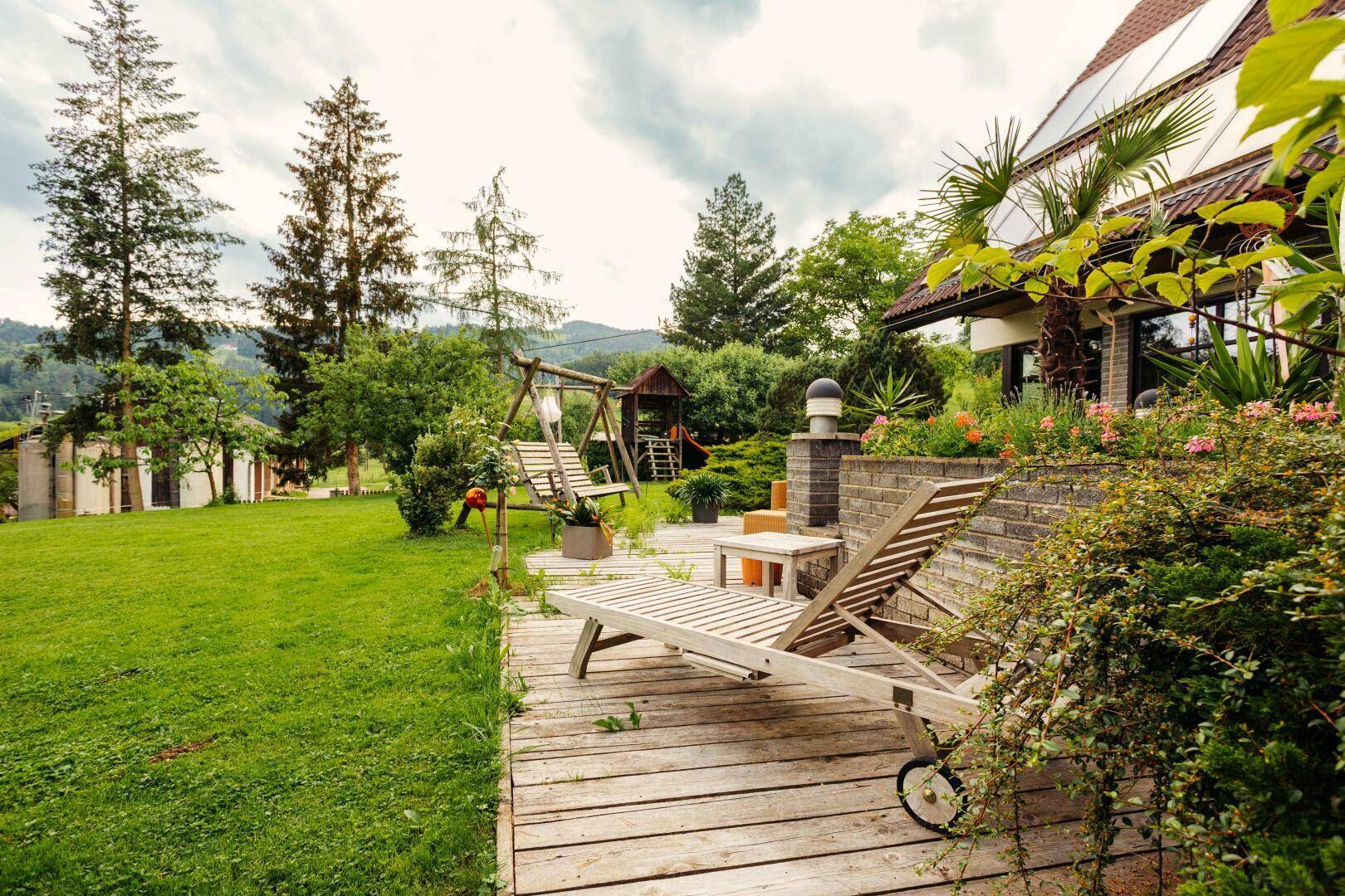 Holzterrasse mit Liegestühlen, angrenzend an eine weitläufige Rasenfläche mit Baumbestand.