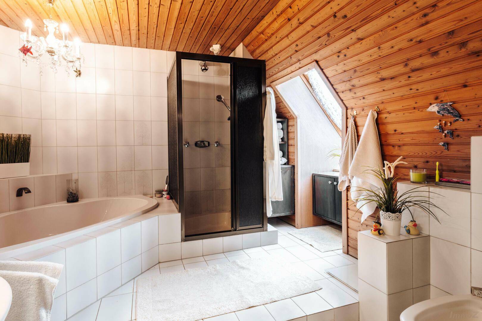 Badezimmer mit Badewanne, Duschkabine und Holzdachschräge, ausgestattet mit weißen Fliesen.
