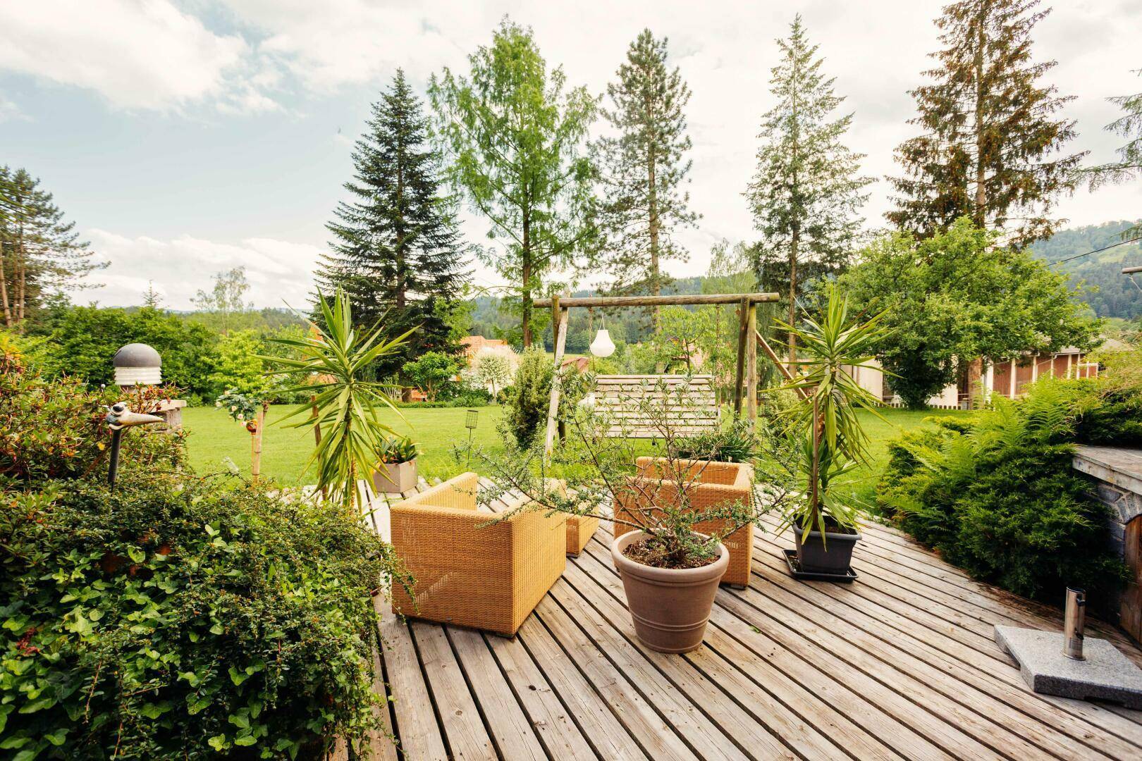 Gemütliche Holzterrasse mit Outdoor-Möbeln und Pflanzen, mit Blick auf den Garten.