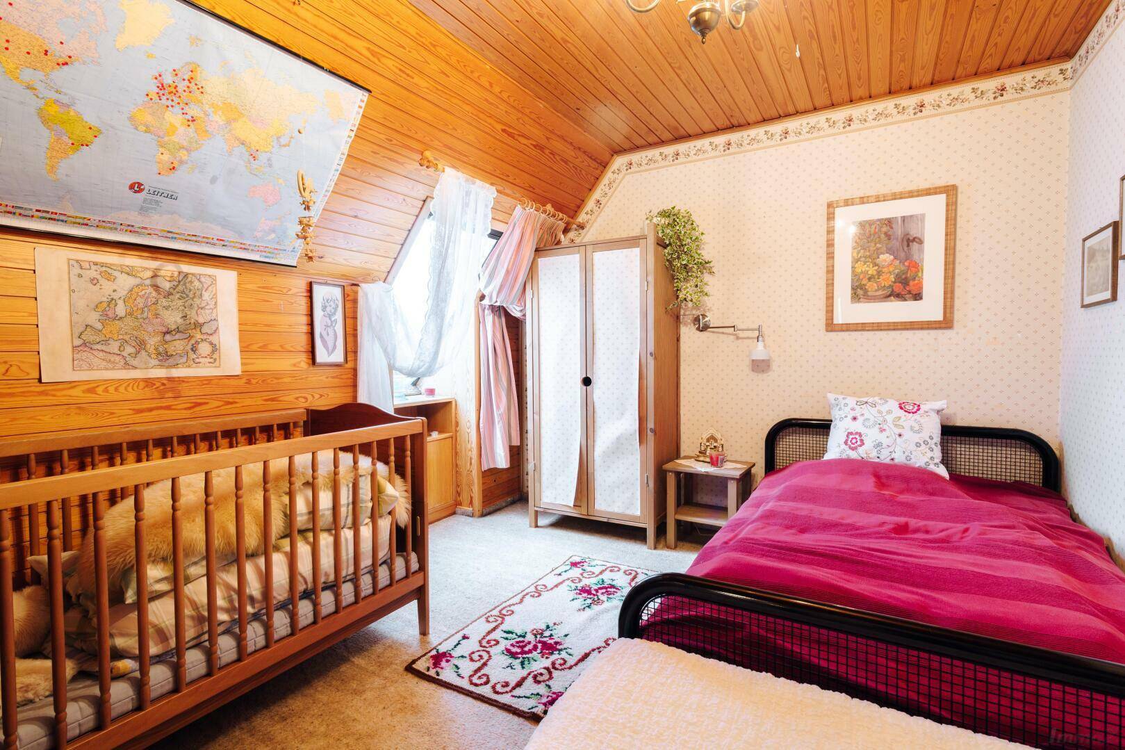 Kinderzimmer mit Babybett, Einzelbett, Holzwänden und -decke, dekoriert mit Weltkarten.