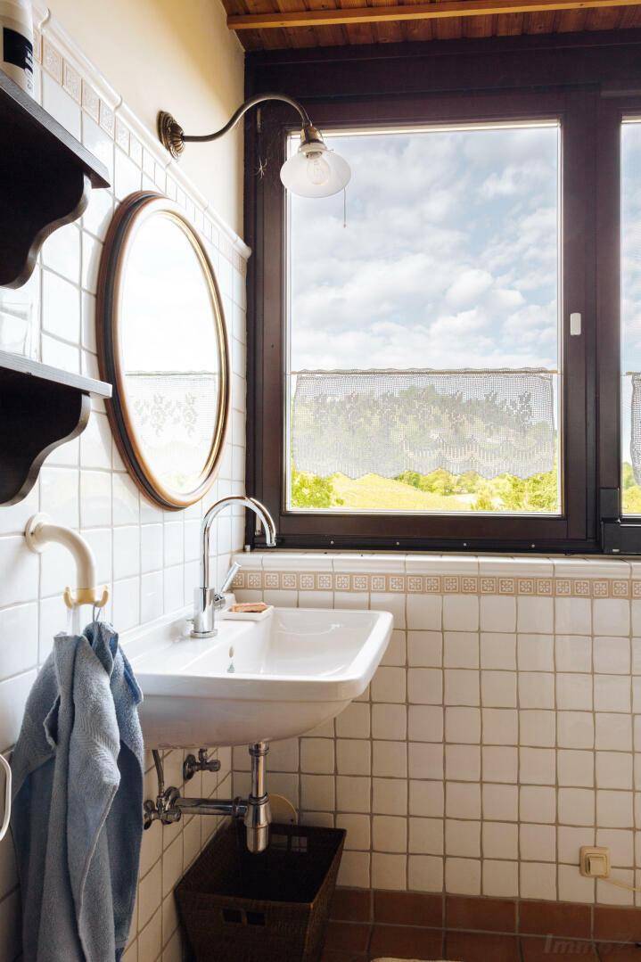 Kleines WC mit Waschbecken und Fenster, das einen Blick ins Grüne bietet.