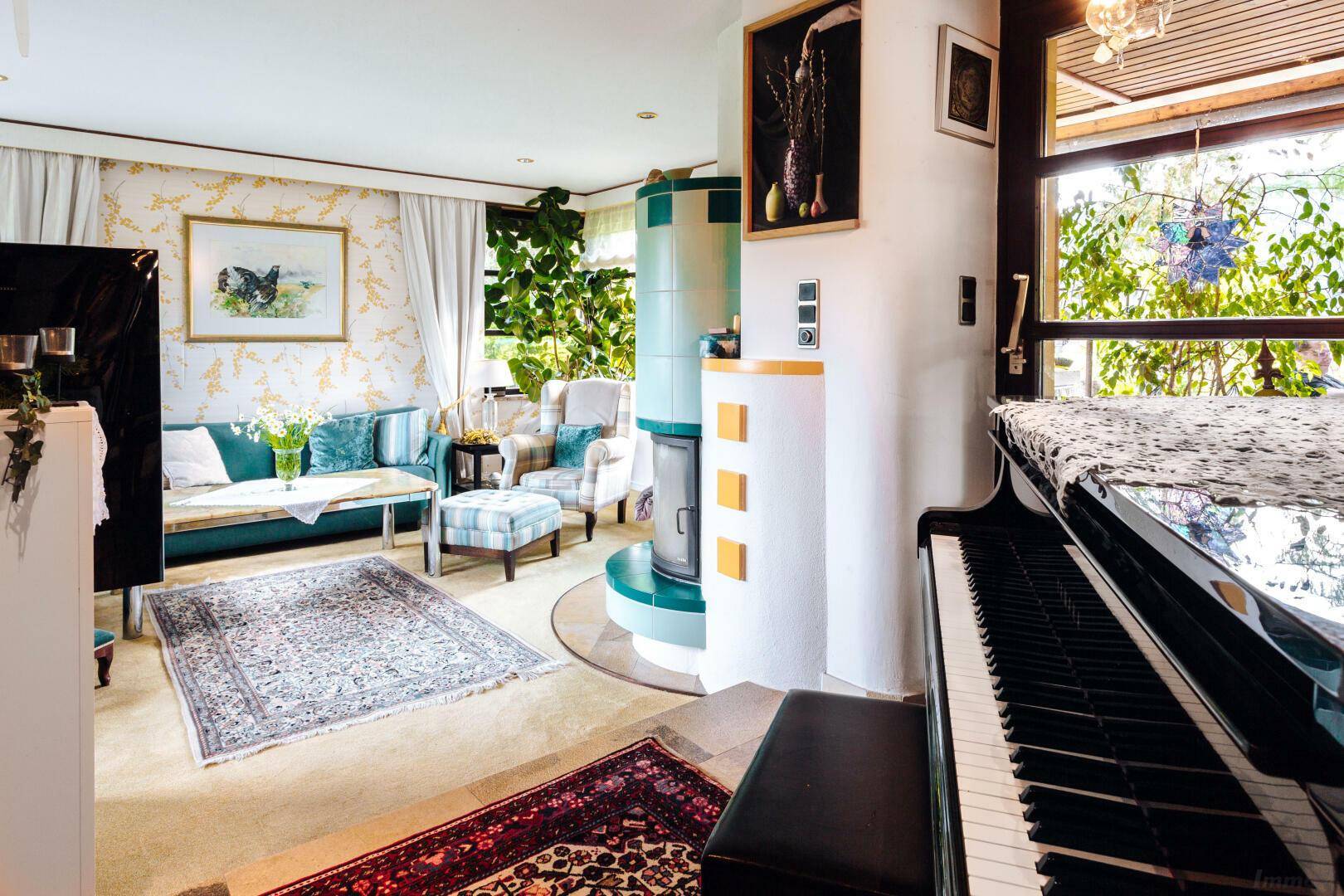 Wohnzimmer mit einem schwarzen Klavier, Kachelofen und Blick in den Garten.