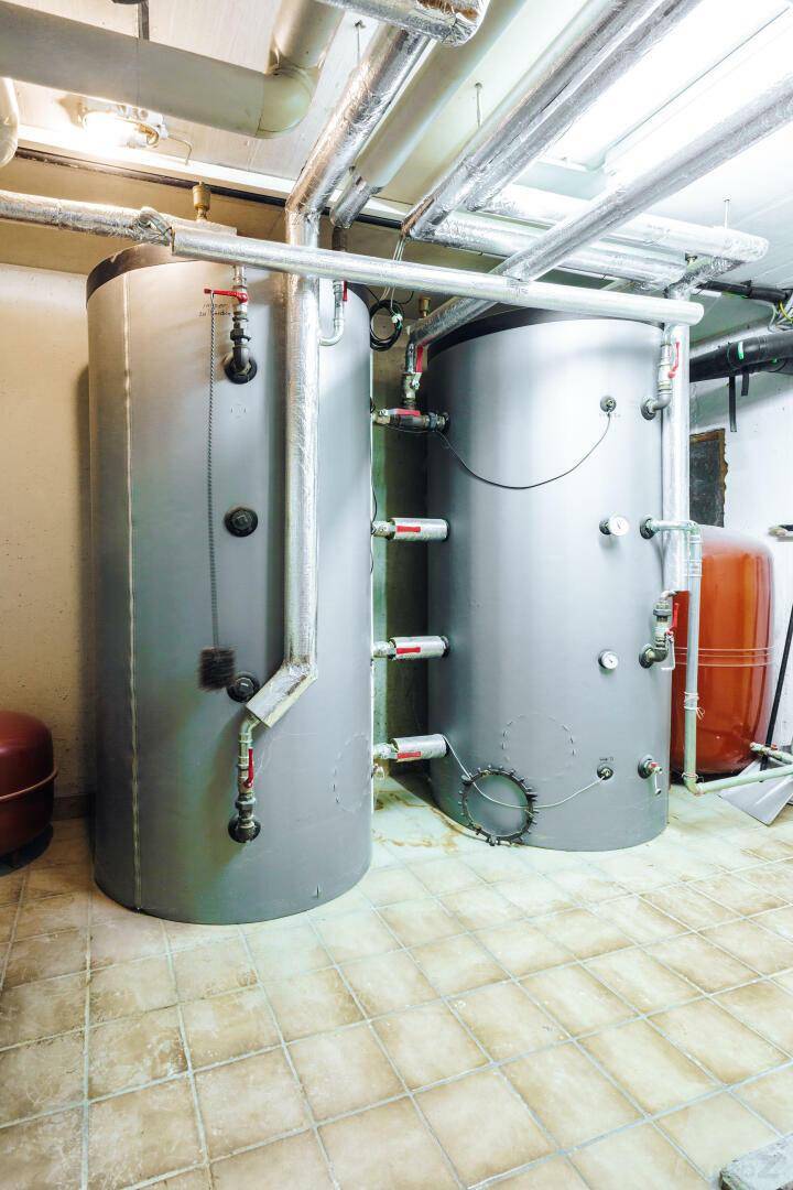 Heizungsraum mit zwei großen Warmwasserspeichern und sichtbaren Rohrleitungen.