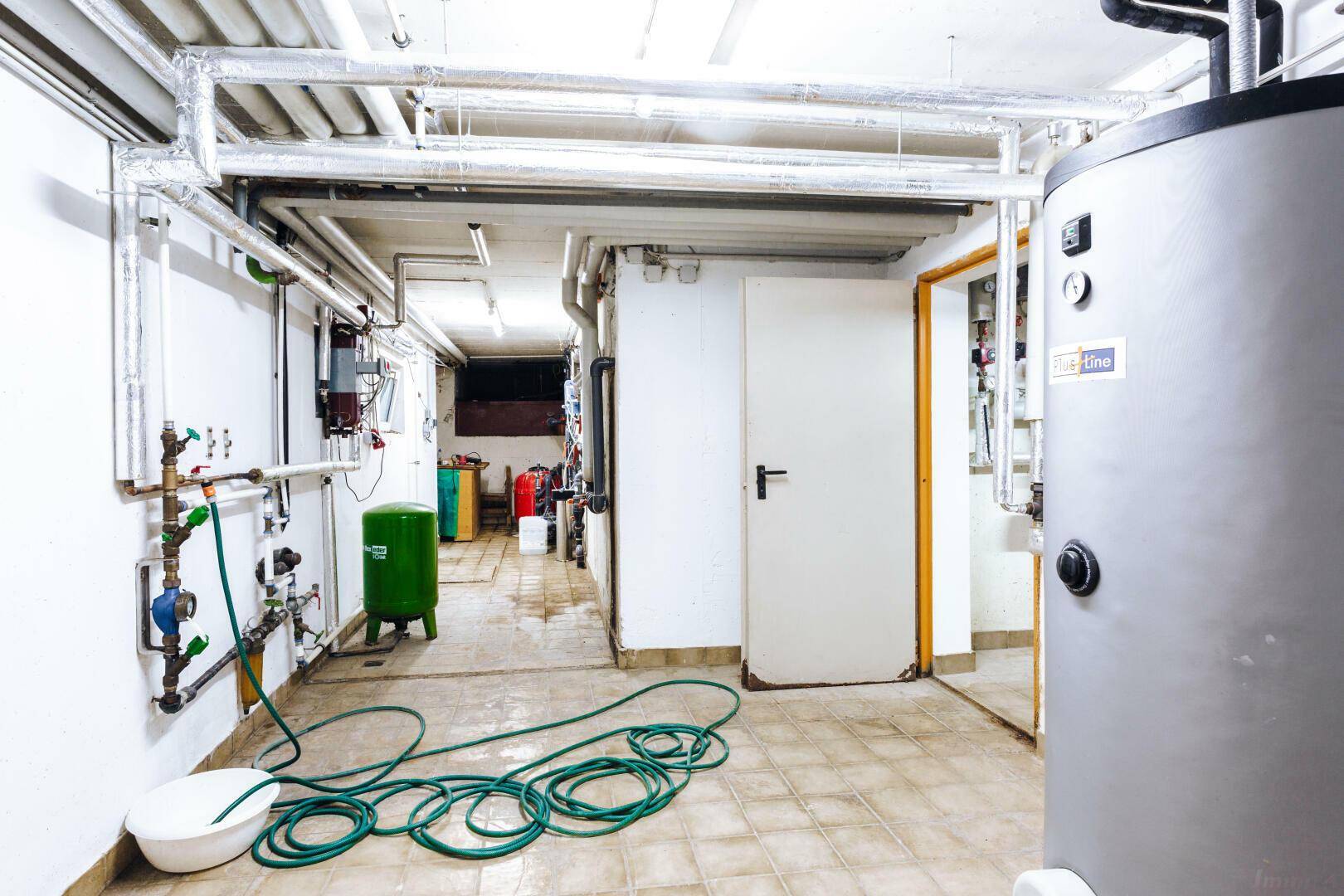 Geräumiger Technikraum im Keller mit umfangreichen Rohrleitungen und Wasseranschluss.