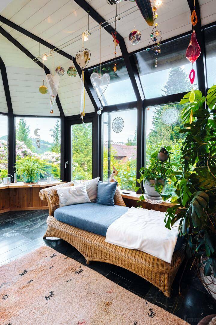 Gemütlicher Wintergarten mit Rattanliege und weitem Blick in den grünen Garten.