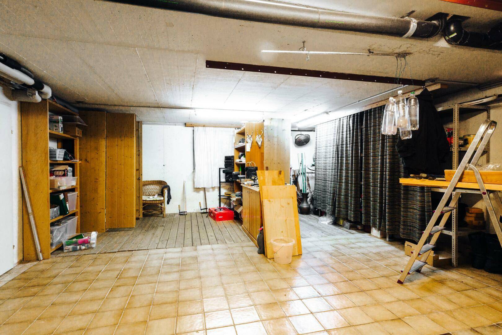 Geräumiger Kellerraum mit Fliesenboden, Regalen und sichtbaren Leitungen an der Decke.