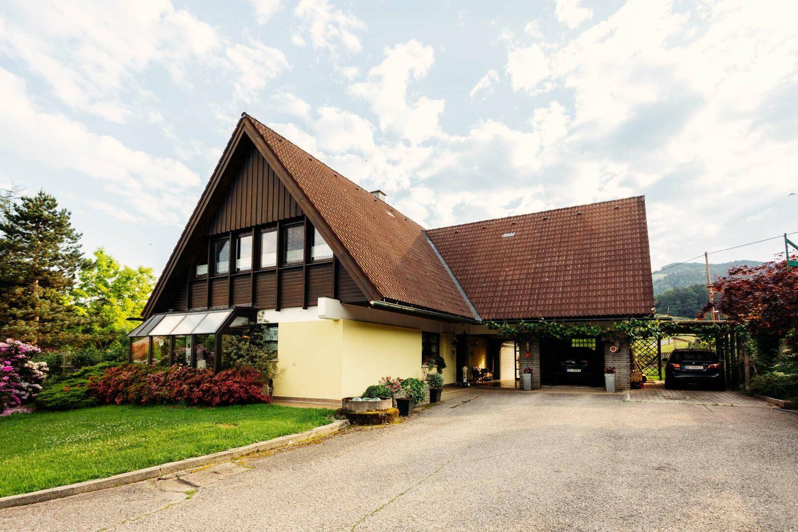 Einfamilienhaus mit markantem Giebeldach, gelber Fassade und integriertem Carport.