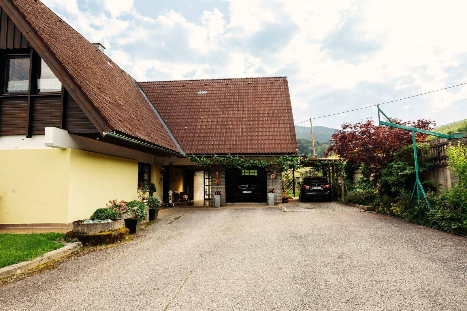 Zufahrt zum Haus mit Carport und Stellplätzen, umgeben von grüner Landschaft.