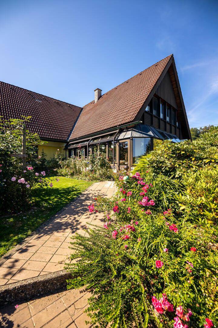 Gepflasterter Gartenweg führt zum Haus mit Wintergarten, umgeben von blühenden Rosen.