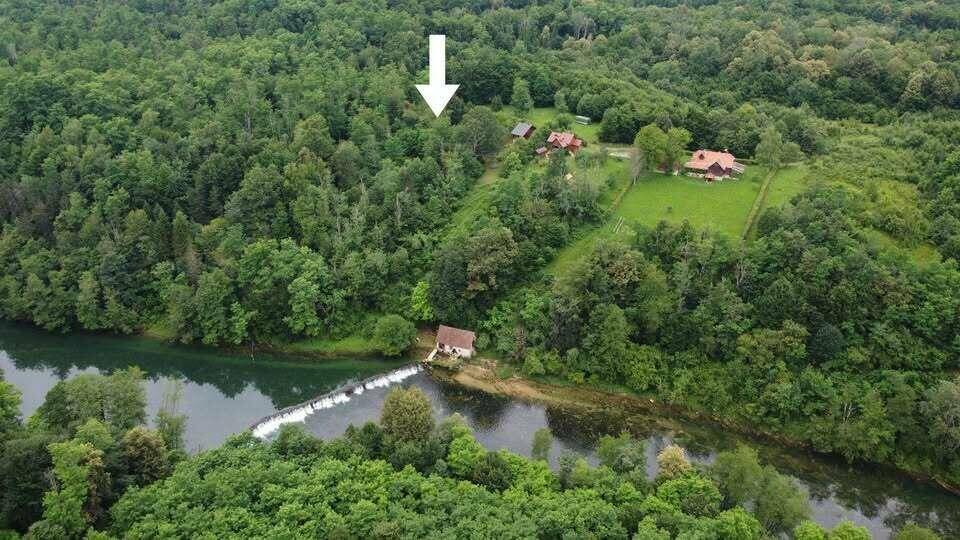 Luftaufnahme einer bewaldeten Flusslandschaft mit Häusern und einem Wehr, die Lage des Anwesens zeigend.