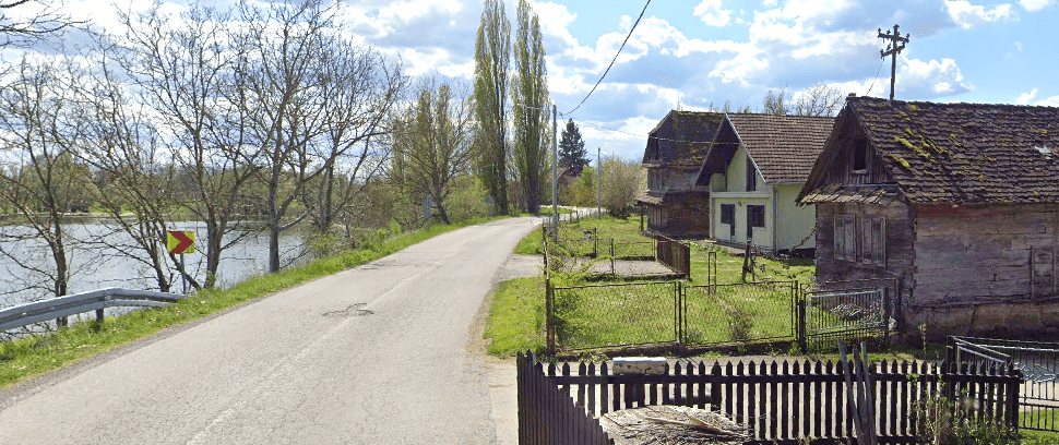 Landstraße führt am Seeufer entlang, mit ländlichen Häusern und einem Holzzaun.