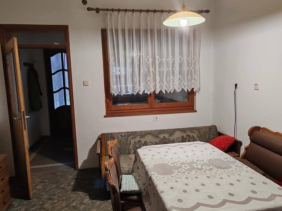 Einfacher Wohn- und Essbereich mit Esstisch, Sofa und Fenster mit Vorhängen.