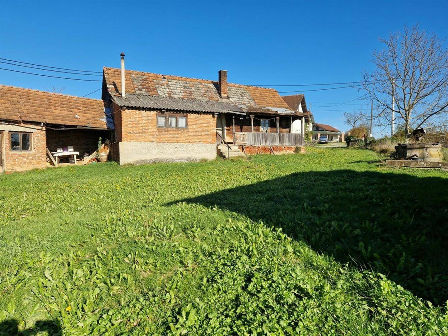 Altes Backsteinhaus mit Ziegeldach und Veranda, umgeben von grünem Rasen unter blauem Himmel.