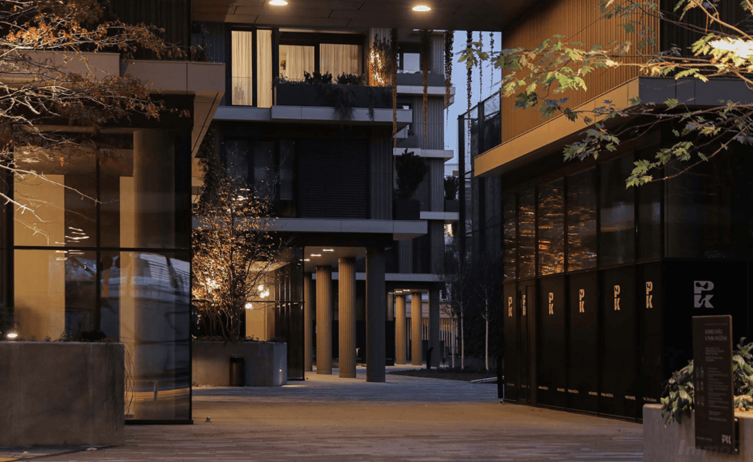 Abendansicht eines modernen Gebäudekomplexes mit beleuchteten Wegen und Fassaden.