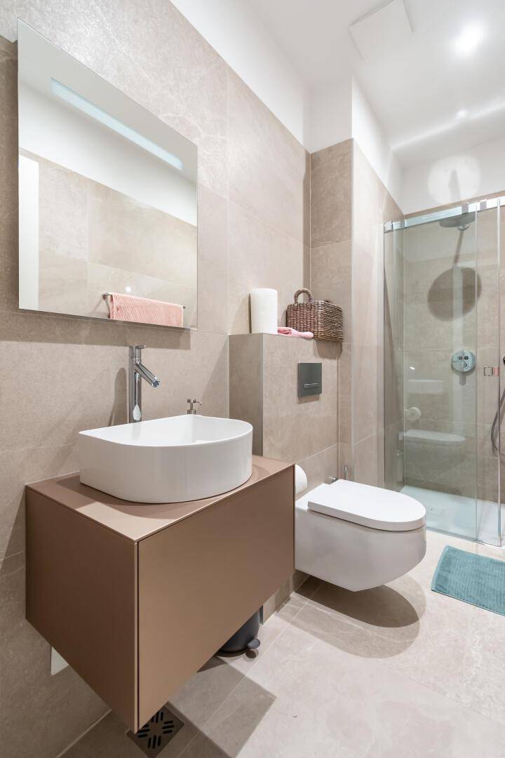Helles Badezimmer mit Einzelwaschbecken, Dusche und beigefarbenen Fliesen.
