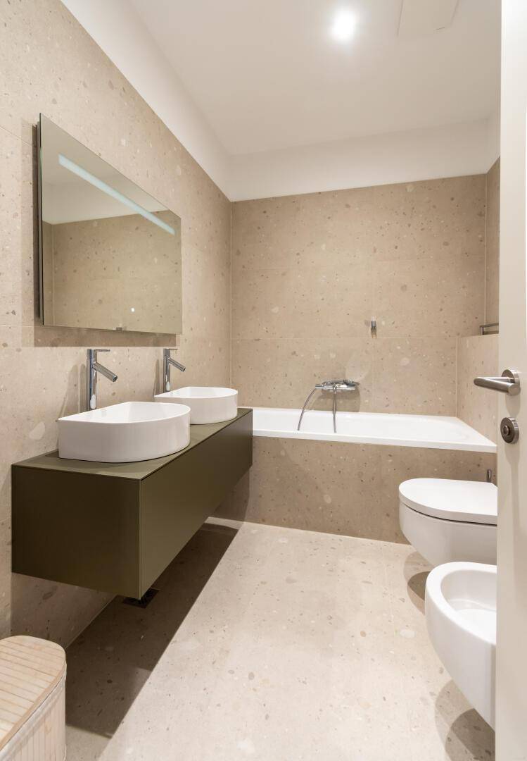 Modernes Badezimmer mit Doppelwaschbecken, Badewanne und beigefarbenen Fliesen.