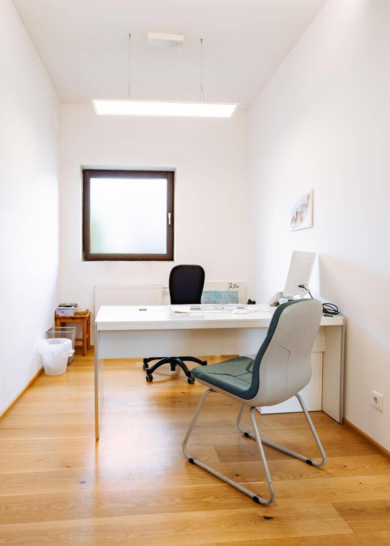 Schlichtes Büro mit Schreibtisch, Bürostuhl, Holzfußboden und einem Fenster.