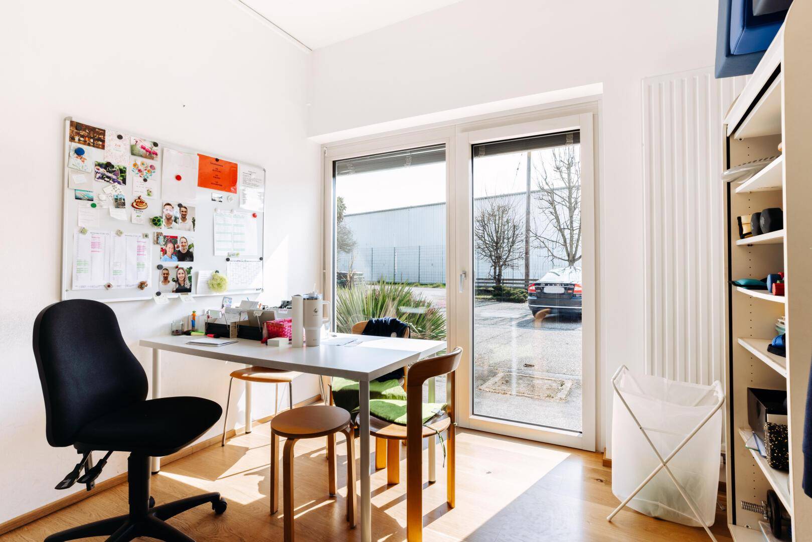 Helles Büro mit Schreibtisch, Bürostuhl, Holzfußboden und großen Fenstern mit Blick nach draußen.