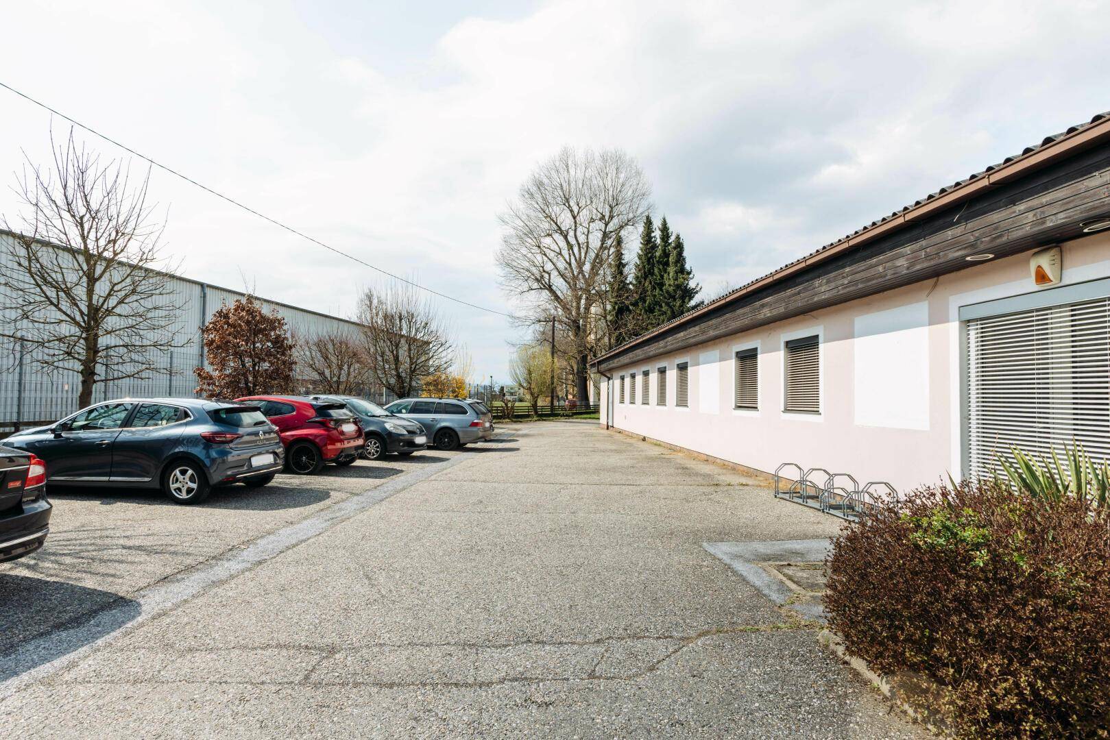 Außenansicht des Gebäudes mit einem großen Parkplatz und Fahrradständern unter bewölktem Himmel.
