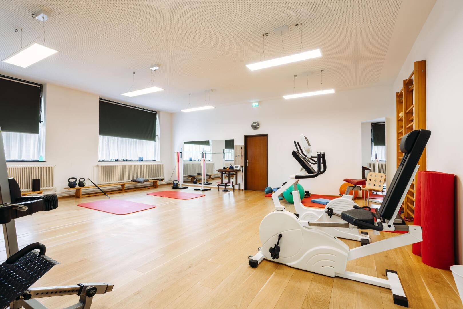 Großer Trainingsraum mit Holzboden, Fitnessgeräten und Sprossenwänden.