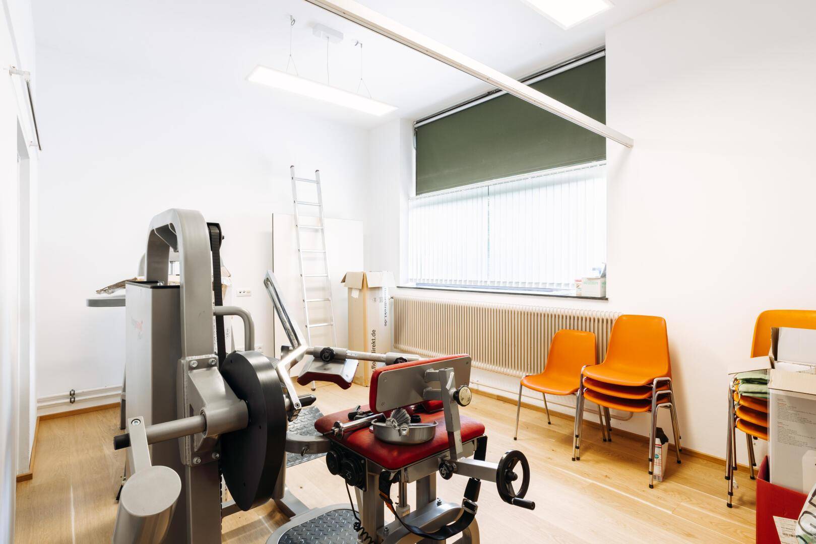 Trainingsraum mit Fitnessgerät, Holzfußboden und einem Fenster mit Jalousien.